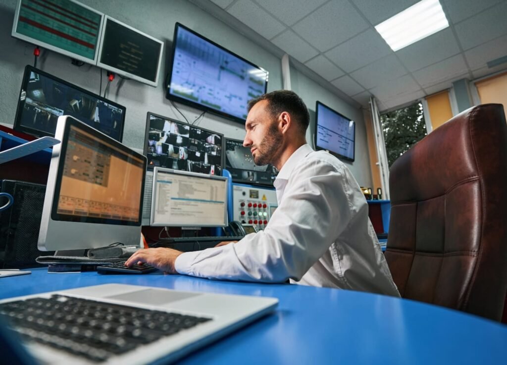 IT technician monitoring systems in a control room with multiple display screens